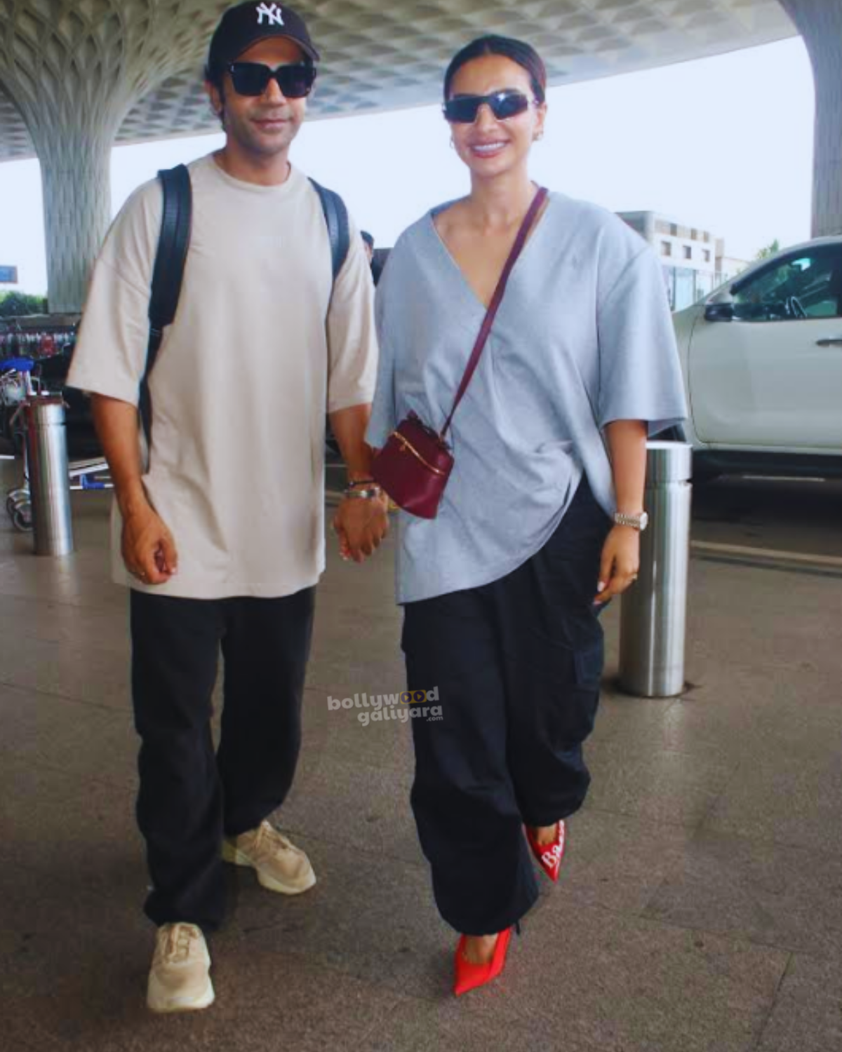 A high-resolution photo of Rajkummar Rao and Patralekhaa walking hand-in-hand at the airport, both dressed in their stylish outfits, smiling and posing for the cameras.